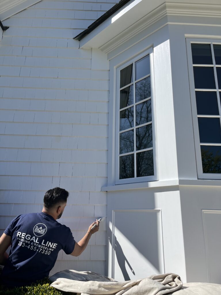 Painter applying fresh white paint to shingle siding and trim on a Darien, CT home exterior