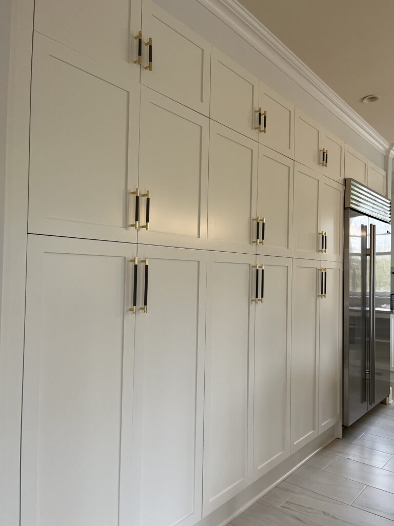 Custom white pantry cabinets in Greenwich, CT with a smooth painted finish, tall shaker panels, and polished brass hardware