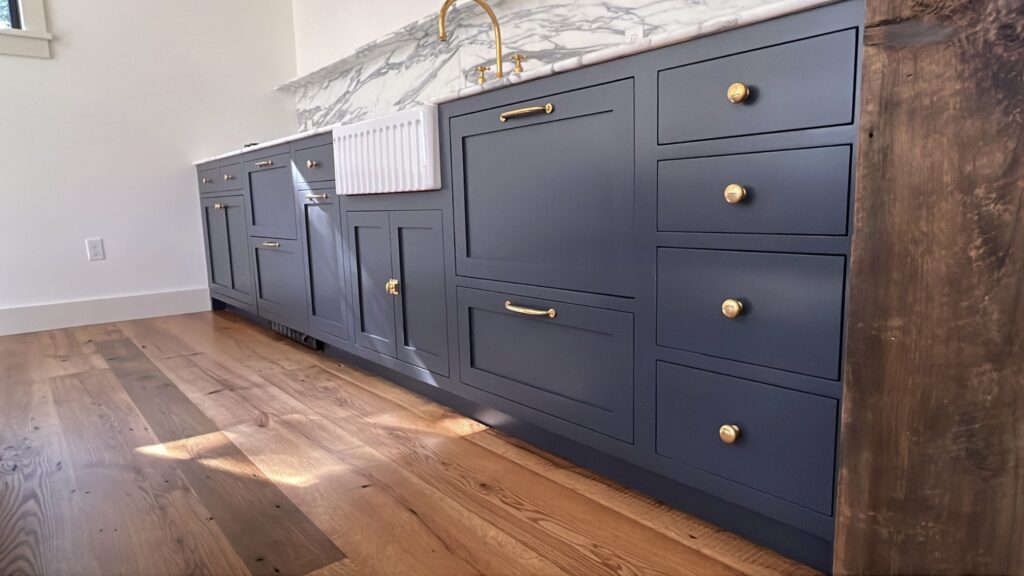 Navy blue kitchen cabinets in Pound Ridge, NY with a smooth refinished finish, brass hardware, and a marble countertop detail