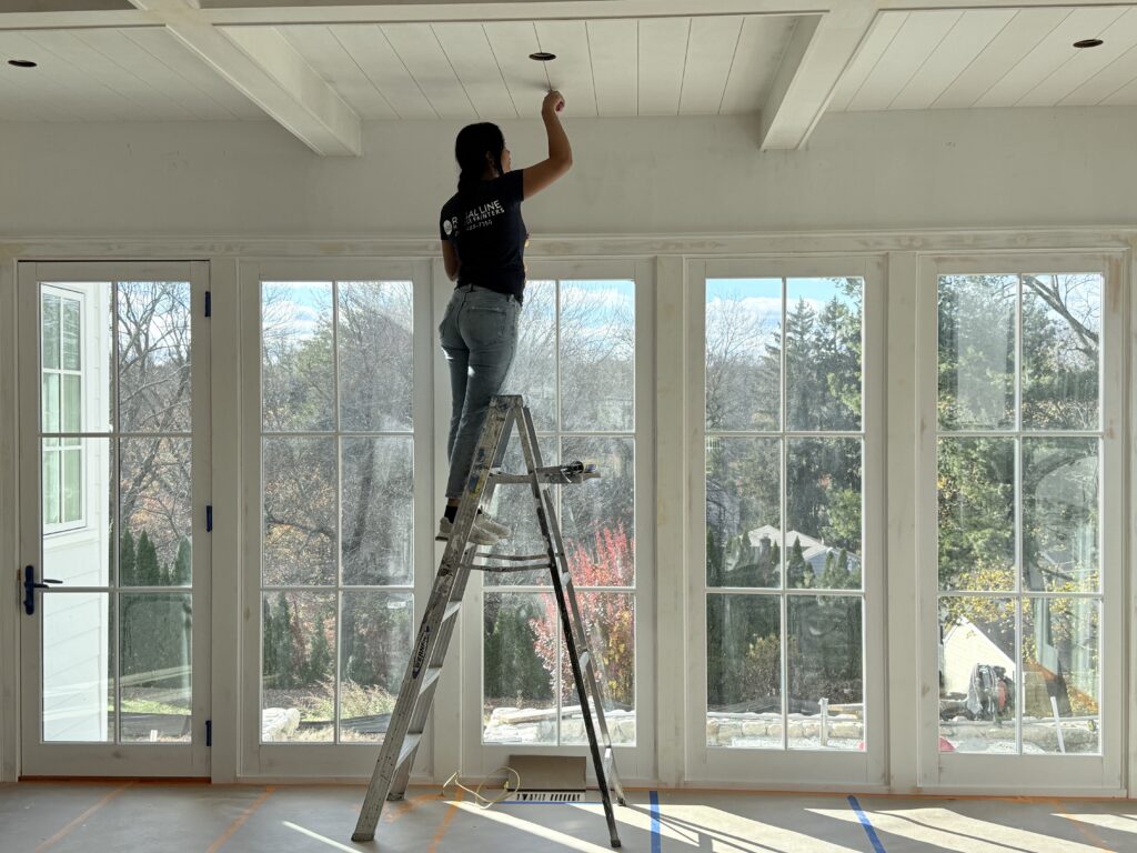 Painter applying fresh white paint to a ceiling and window wall in Westport, CT with tall glass panels and bright natural light