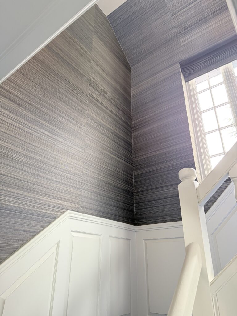 Textured wallpaper detail in Bedford, NY with dark horizontal patterning, crisp white paneling, and a bright stair wall corner