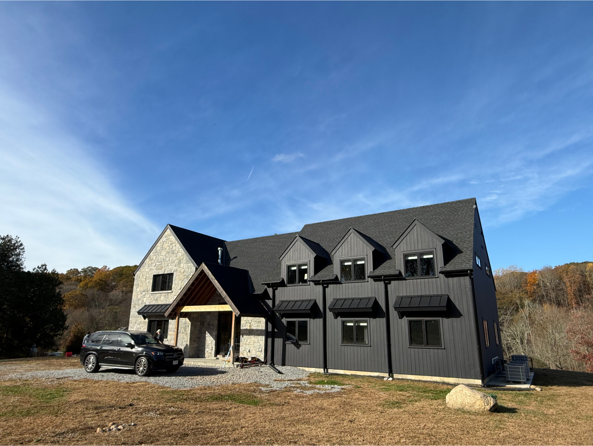 Exterior painting project in Bedford, NY featuring a dark exterior home with vertical siding, black trim accents, and stone façade details