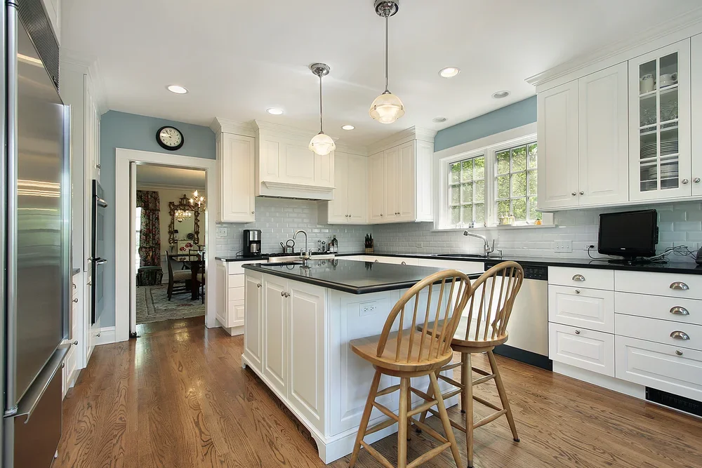 Bright kitchen in Darien, CT with soft blue walls, white cabinetry, black countertops, and a clean painted finish
