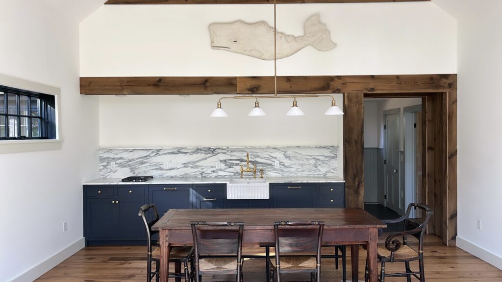 Navy guest house cabinetry in Pound Ridge, NY with a marble backsplash, farmhouse sink, and warm wood beam detailing